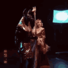 a woman is standing next to a statue of an anubis holding a staff