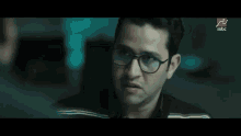 a man wearing glasses is talking to another man in a dark room