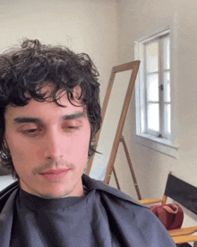 a man with curly hair is sitting in front of a window