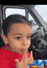 a young boy in a red shirt is sticking his tongue out while sitting in a car