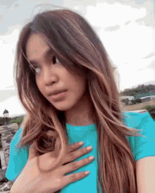 a woman with long hair is wearing a blue shirt and holding her hands to her chest .