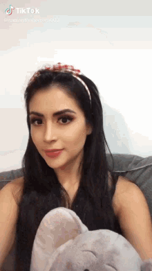 a woman wearing a headband is sitting on a couch holding a stuffed animal ..