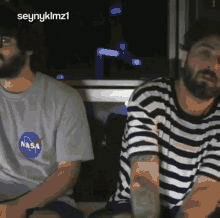 a man wearing a nasa shirt is sitting next to another man