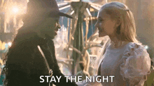 a man and a woman are standing next to each other in front of a carousel and the man is telling the woman to stay the night