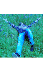 a man in a plaid shirt is laying in a field of grass with his arms outstretched