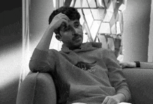 a man wearing a hollister sweatshirt sits in a chair