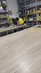a man in a yellow shirt with the letter t on it sits at a desk in a store