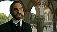 a man with a beard wearing a suit and tie stands in front of a building .