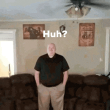 a man is standing in a living room with his hands in his pockets and the words huh on the wall .