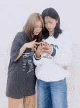 two girls are looking at a cell phone together .