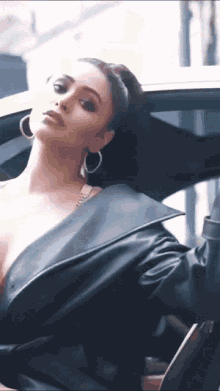 a woman in a black leather jacket and hoop earrings is sitting in a car