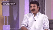 a man with a mustache wearing a striped shirt is sitting on a chair .