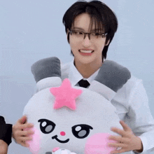 a young man wearing glasses is holding a stuffed animal with a pink star on it .