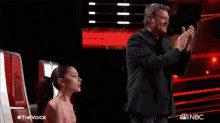 a man in a suit applauds while a woman in a pink dress looks on ..