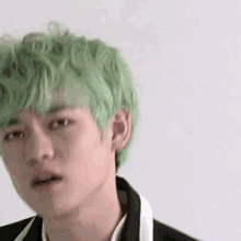 a young man with green hair is wearing a black jacket and a white shirt .