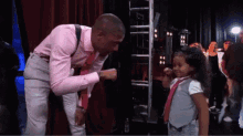 a man in a pink shirt and tie is talking to a little girl in a tie .