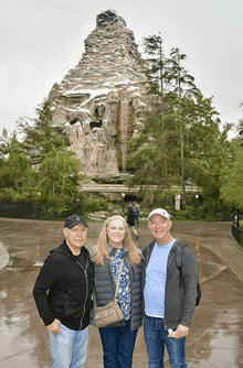 three people standing in front of a mountain with a waterfall