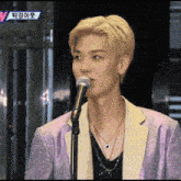 a man in a purple jacket is singing into a microphone on a television screen