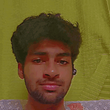a young man with a beard looks at the camera with a yellow background