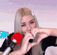 a woman is making a heart shape with her hands in front of a red microphone .
