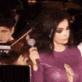 a woman in a purple dress is holding a microphone in front of a group of people .