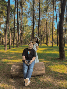 a man sits on a log while a woman stands behind him in a park