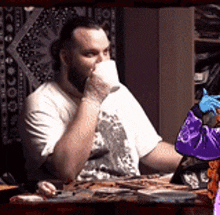 a man is drinking from a cup while sitting at a table