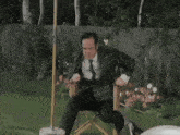 a man in a plaid shirt and tie is sitting in a chair in a garden