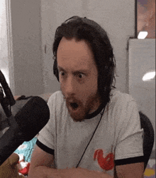 a man with a beard wearing headphones is sitting in front of a microphone making a surprised face .