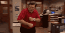 a man in a red shirt and black pants is dancing in an office