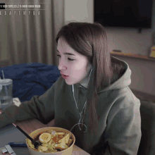 a woman in a green hoodie is eating a bowl of food