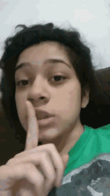 a woman in a green shirt is holding her finger to her lips