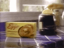 a box of eggs sits on a tiled counter next to a jar of syrup .