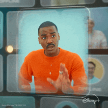 a man in an orange sweater is standing in front of a disney+ screen