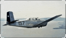 a small plane with the number 157 on the side is flying over the ocean .
