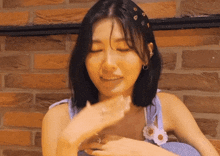 a woman is sitting in front of a brick wall and covering her face with her hands .