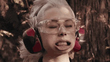 a woman wearing ear muffs and safety goggles sticks her tongue out