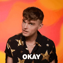 a man wearing a black shirt with gold stars and the word okay below him