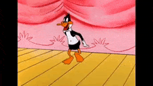 daffy duck is dancing on a stage with a pink curtain behind him .