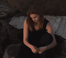 a woman in a black dress is sitting on a wooden dock .