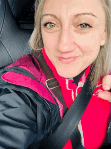 a woman wearing a black jacket and a pink shirt has a black seat belt around her neck