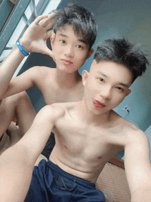 two shirtless boys are posing for a picture with one wearing a blue wristband that says ' a ' on it