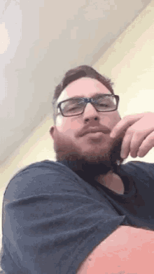 a man with a beard wearing glasses and a black shirt is looking at the camera .