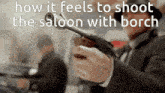 a man in a suit is holding a gun in his right hand and says how it feels to shoot the saloon with borch .