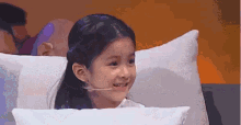 a little girl is sitting on a bed with a white pillow .