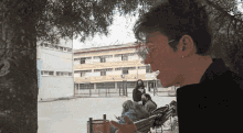 a man smoking a cigarette in front of a building with a few people sitting on benches