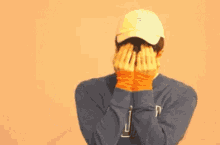 a person wearing a hat and a blue sweater is covering their face with their hands .