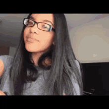 a woman wearing glasses and a gray shirt is making a funny face .