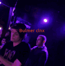 a man stands in front of a crowd with the name bulmer clnx on the bottom right