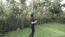 a woman in a black shirt is standing in a grassy yard holding a cell phone .